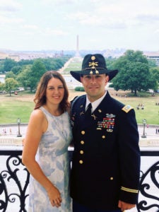 Christopher and Betsey Mercado stand beside each other outside with the Washington Monument off into the distance.