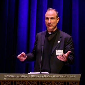 Msgr. Melchor Sanchez de Toca at a podium reading National Museum of African American History and Culture. 