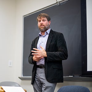 Adam Rothman stands in a classroom in front of a blackboard