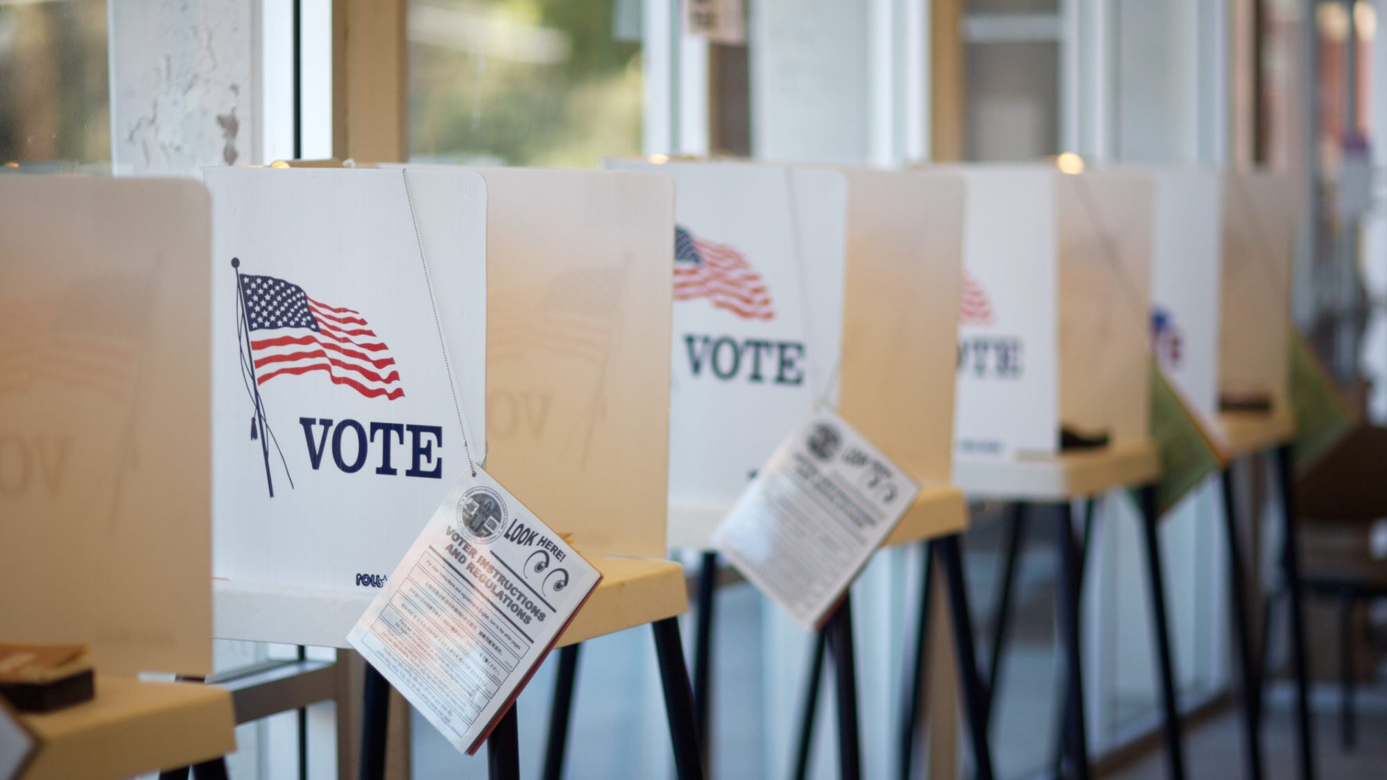 Voting booths lined up with the word &quot;vote&quot; and an American flag on them and a ballot information attached