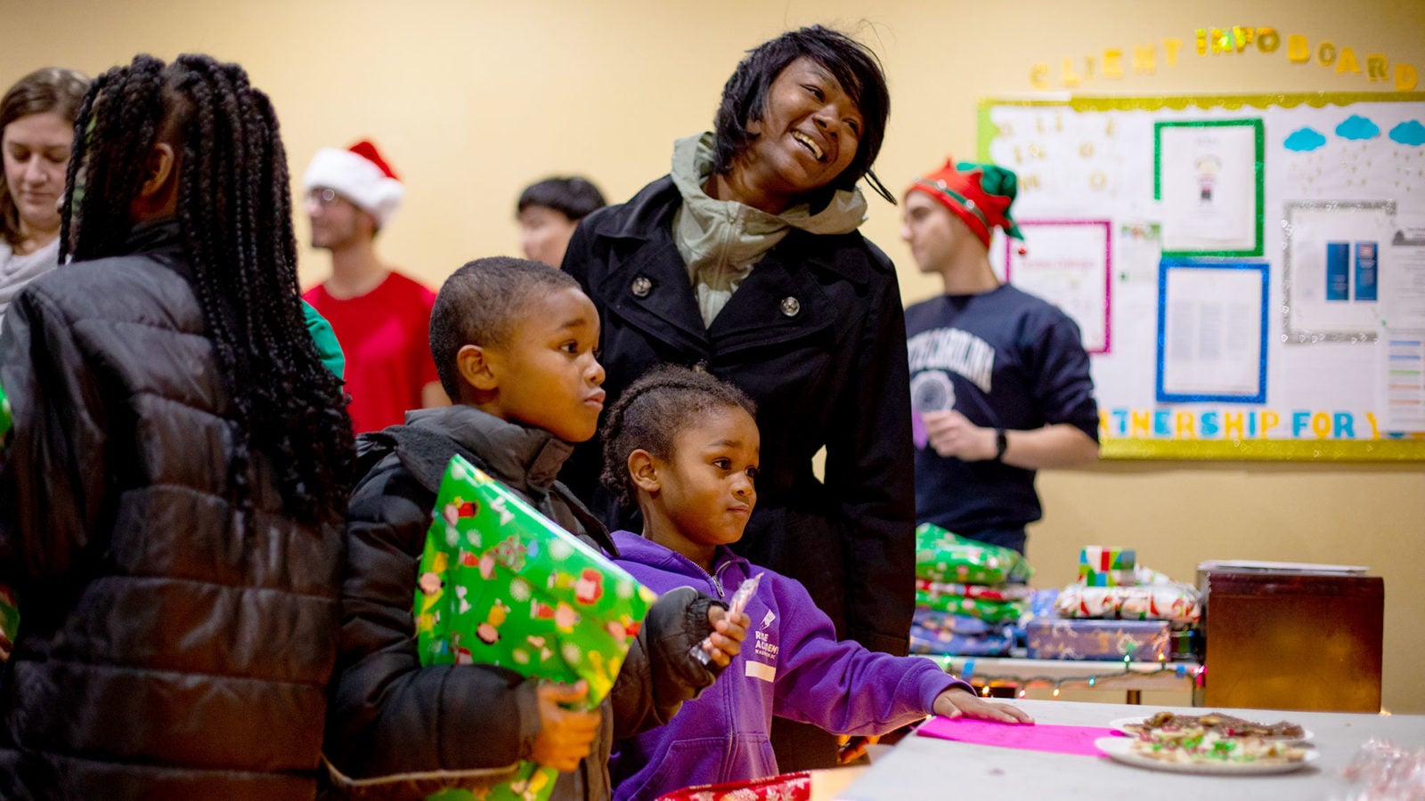 A woman smiles with her two children as they hold wrapped Christmas presents.