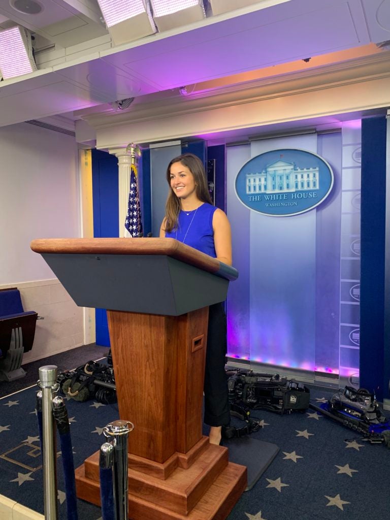 Student smiles while standing behind a podium in the White House briefing room.