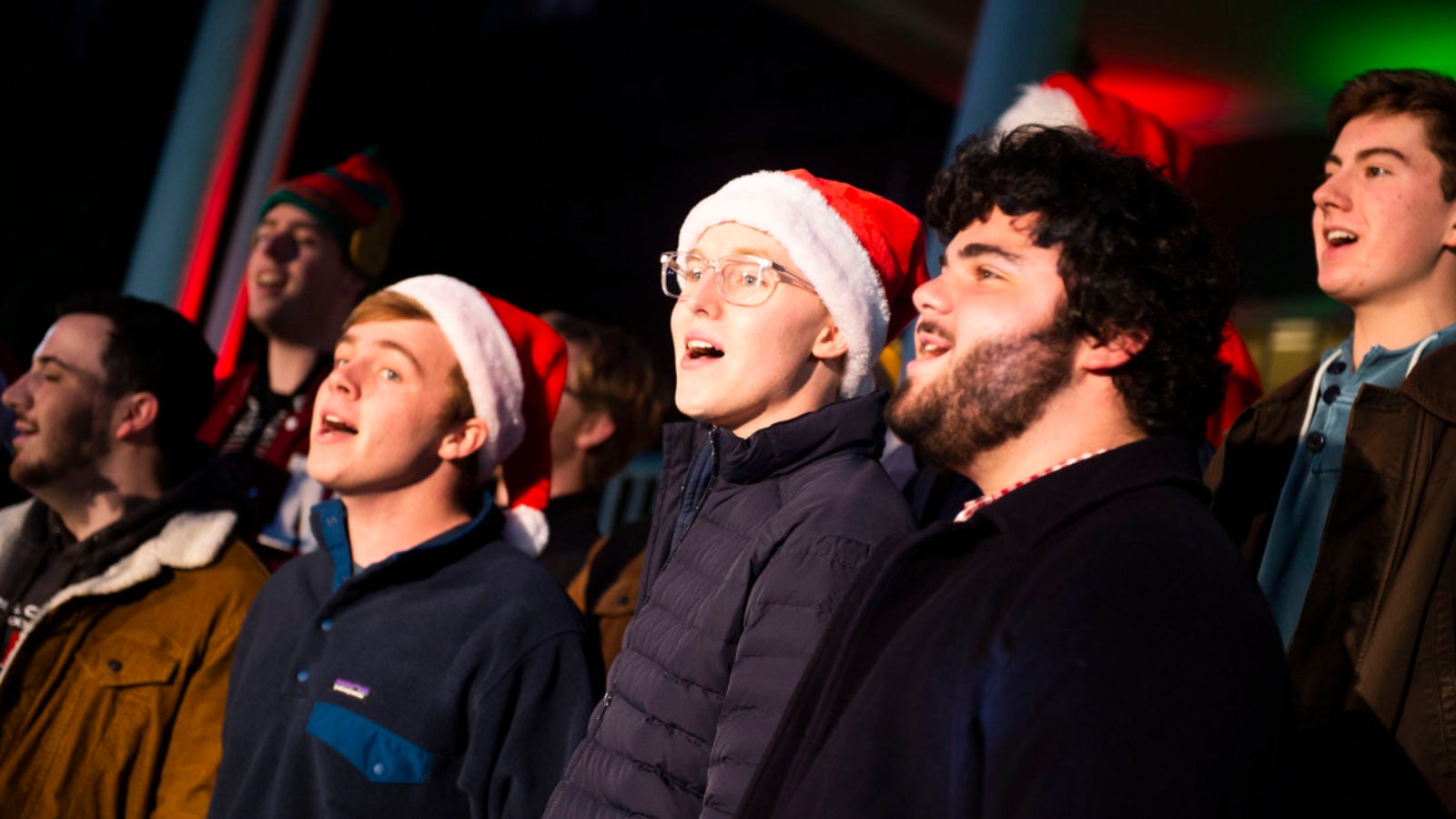 Students sing in chorus outside donning Santa hats during an evening performance.