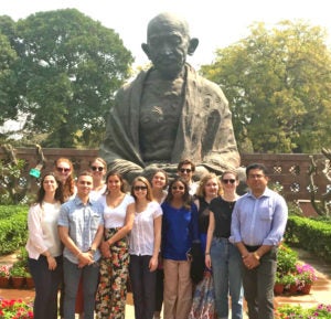 A group of people, including Kyra Kocis, in front of a statue of Gandhi.