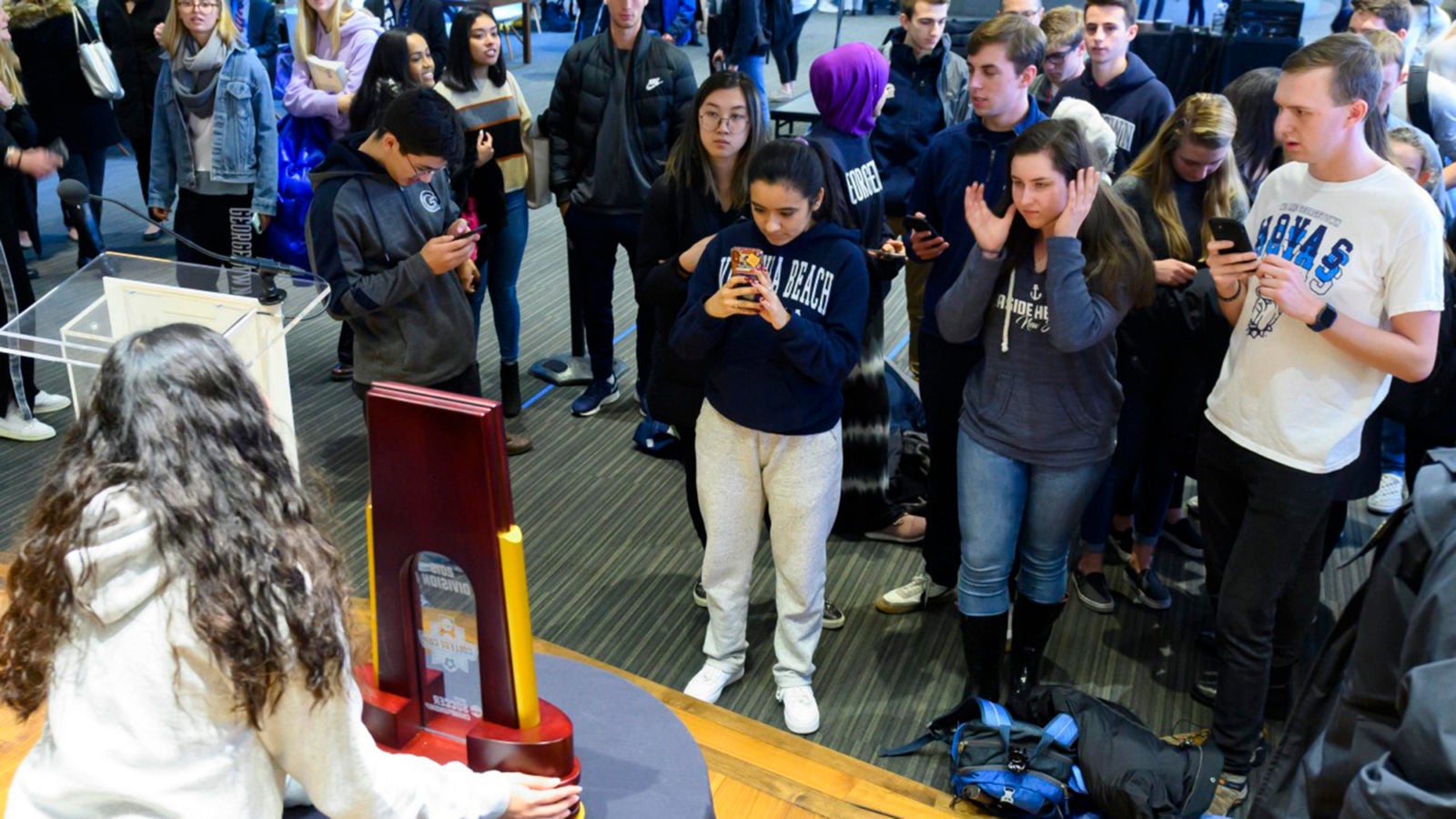 Georgetown students stand and take photos of the NCAA Championship trophy held by a woman on a stage