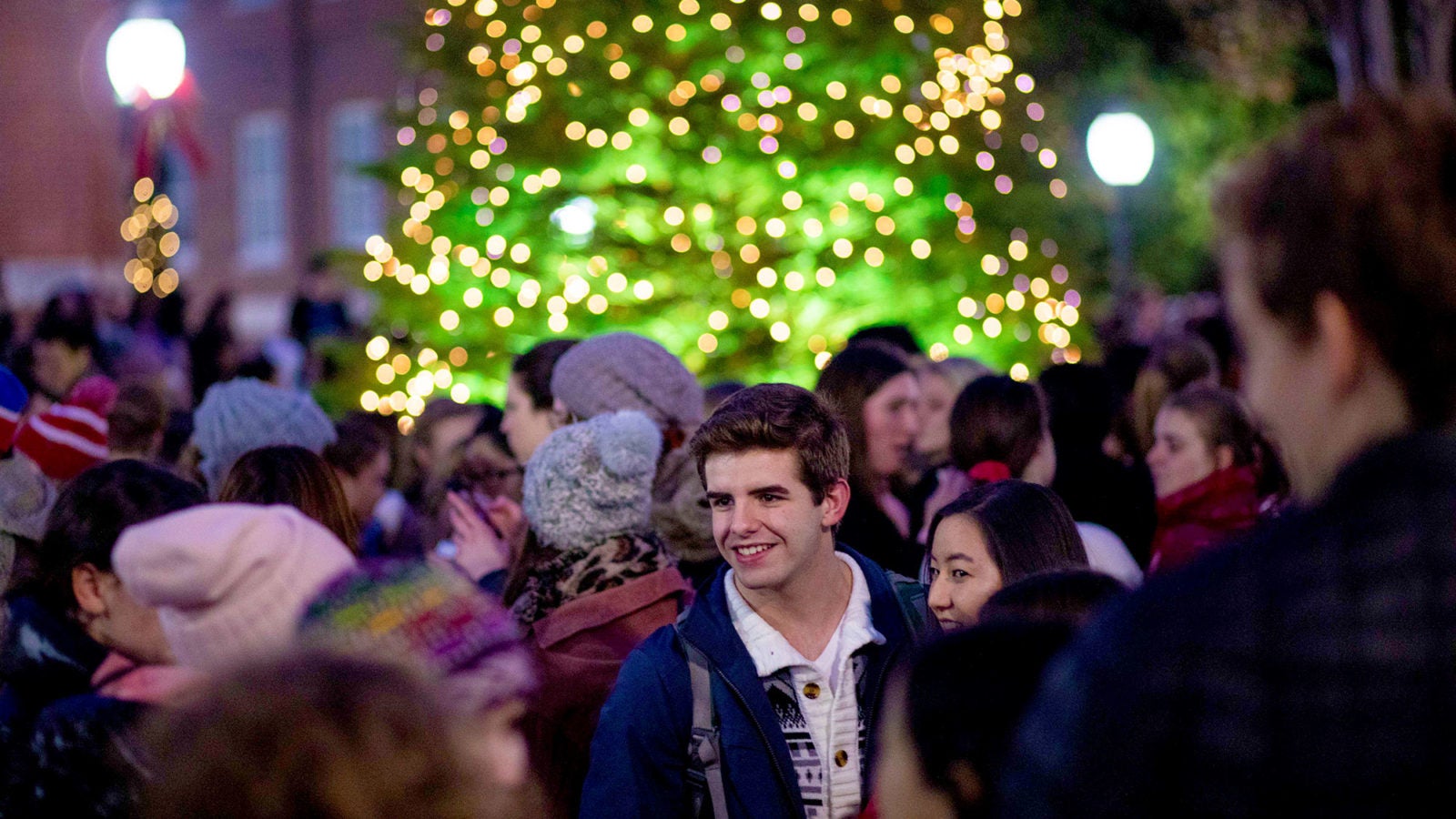 Students talk outside with a lit Christmas tree in the background.