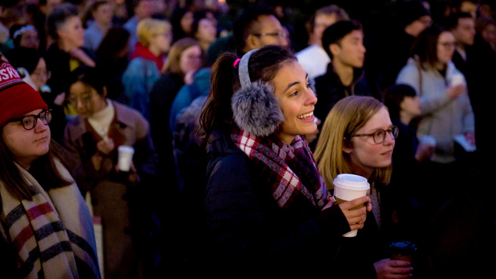 A female student looks at a performance with a smile amid a crowd of students.