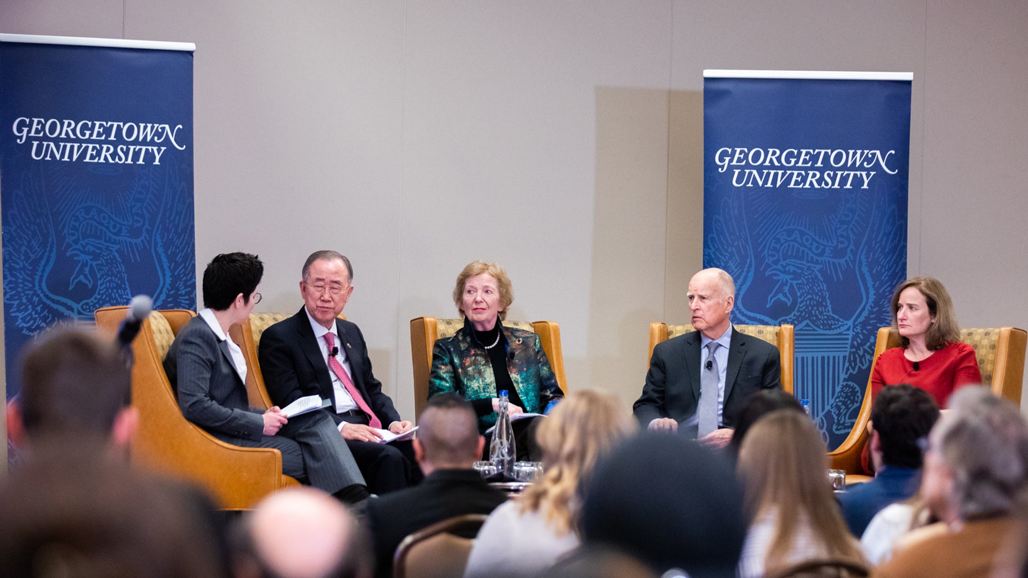 Desha Girod holds a microphone sitting next to Ban Ki-Moon, Mary Robinson, Jerry Brown and Rachel Bronson with a Georgetown University banner behind them