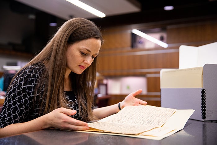 Cassandra Berman sits at a desk looks through a manuscript from the 1800s