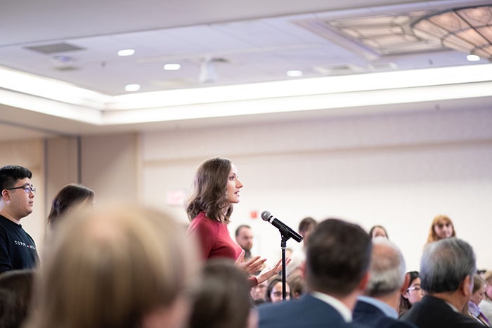 Jessica Rogers standing at a podium with others sitting in chairs.