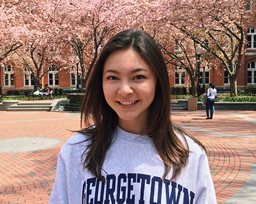 Michelle Renslo wearing a Georgetown sweatshirt outside with cherry trees in bloom behind her