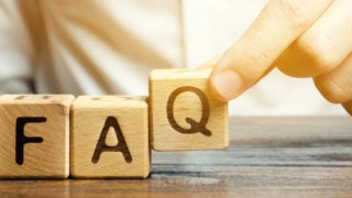 Person puts wooden blocks with the word FAQ (frequently asked questions).