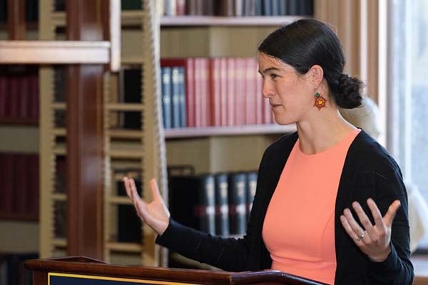 Joanna Williams gesturing with bookshelves behind her in Riggs Library