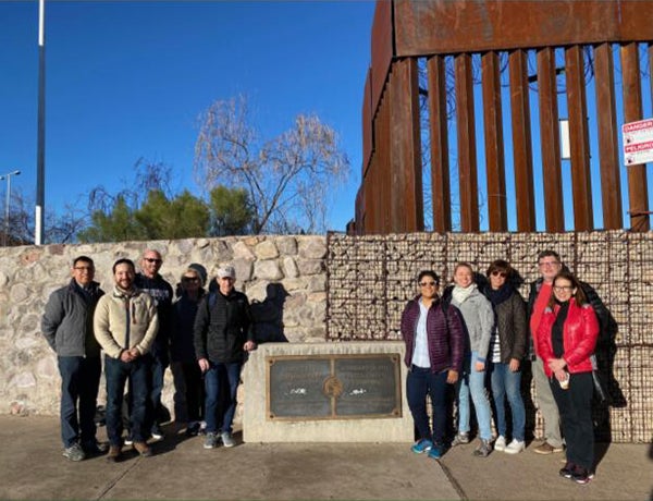 Georgetown faculty and staff stand on either side of a plaque in front of the wall at the border of the U.S. and Mexico