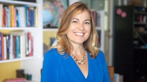 Andrea Bonoir stands in front of a bookcase smiling at the camera.