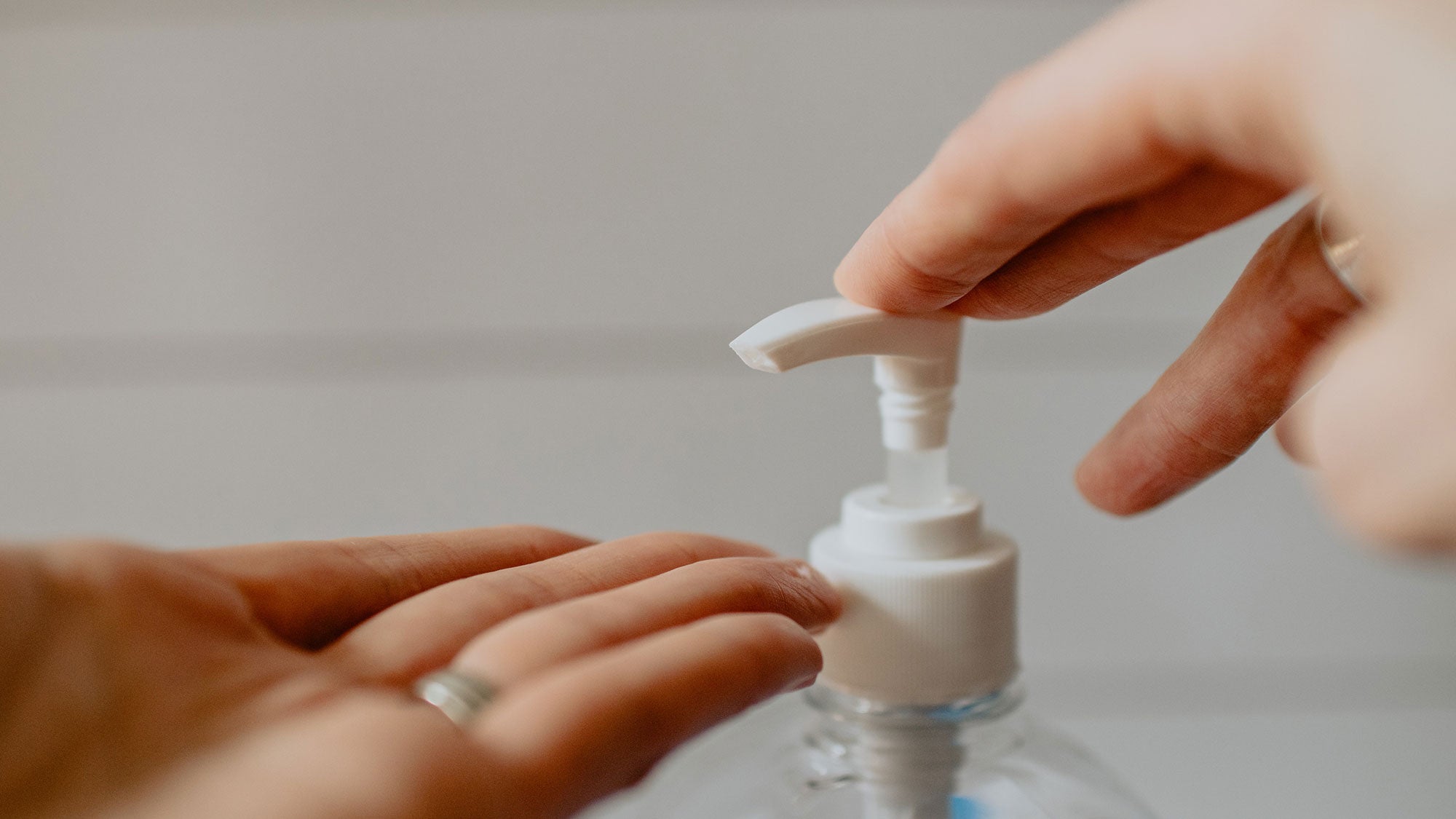 Hands push the top of a hand sanitizer dispenser.