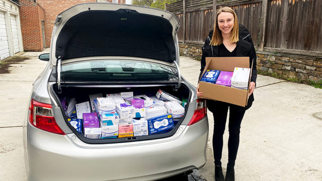 Allison Rooney holds a box of medical supplies next a car whose trunk is full of such supplies.