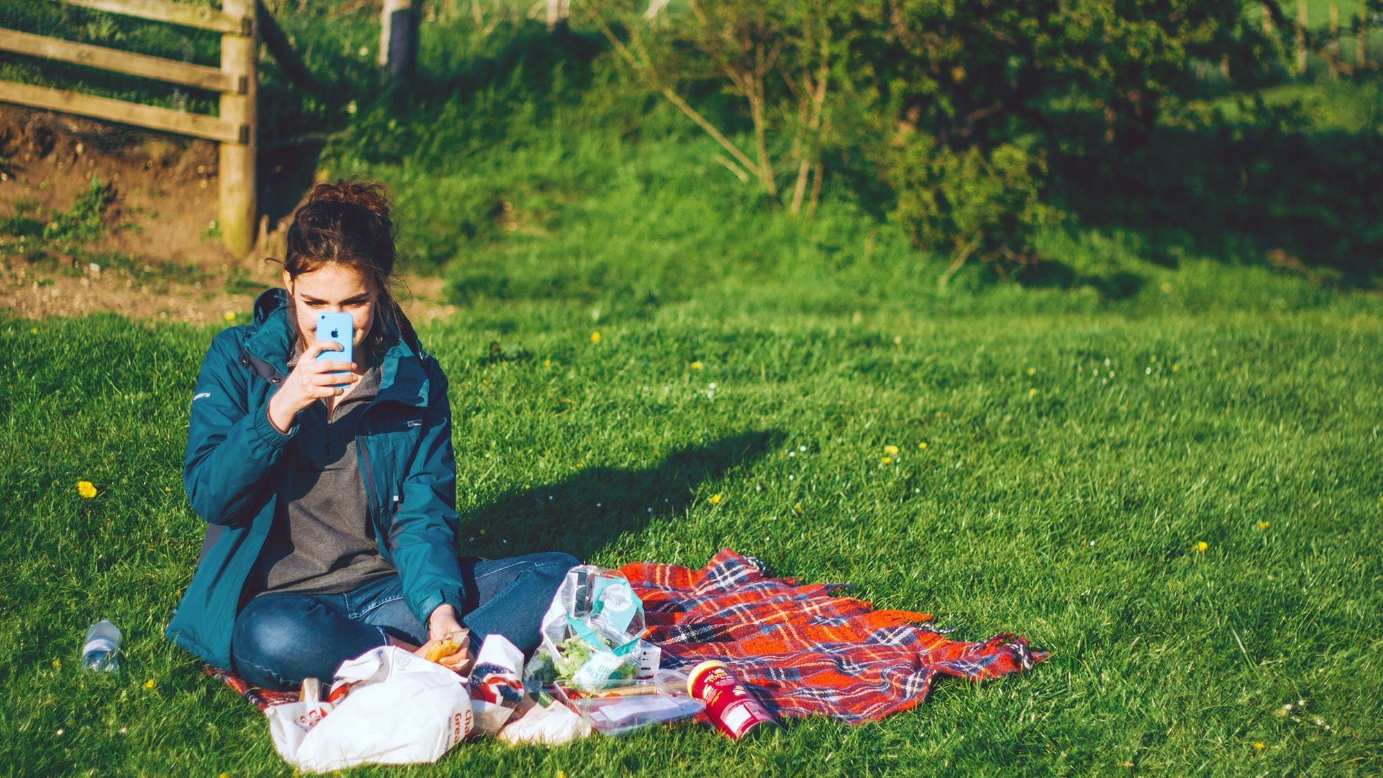 A woman sits outside in the grass chatting by video on her phone.