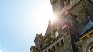 The sun peeks out from the corner of an opening between Healy Hall and the sky.