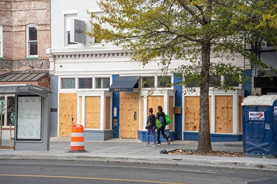 Two people walk by a boarded up restaurant