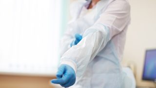 A health professional wearing gloves pulls on a protective gown