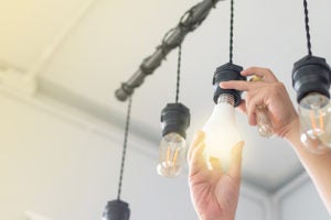 Hands screwing in a hanging light bulb, with other hanging bulbs.