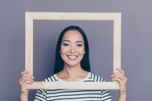 Closeup of young woman holding an empty picture frame in front of her face