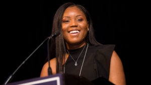 Taurjhai Purdie speaks into a micrphone as she stands at a lectern.