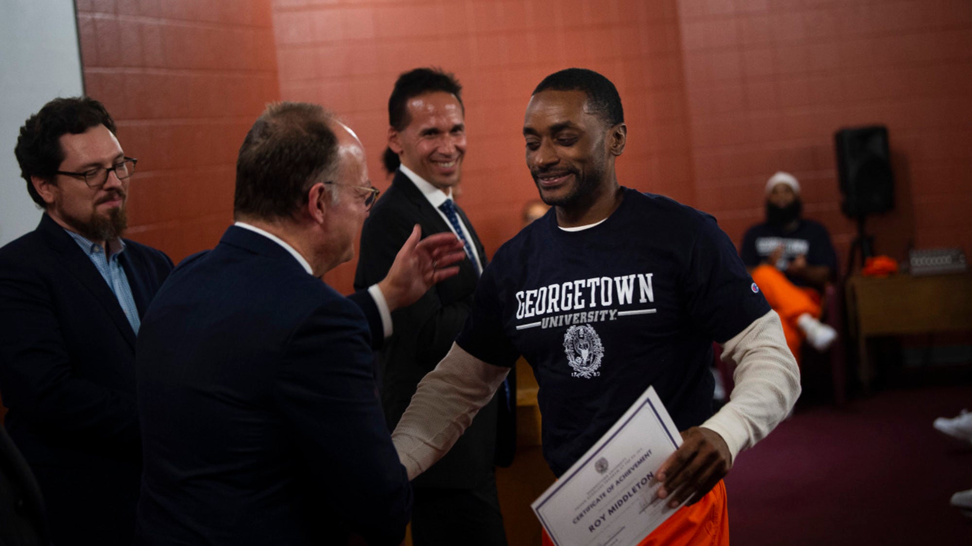 Roy Middleton holds his certificate of achievement while shaking hands with President DeGioia as Marc Howard and Josh Miller look on