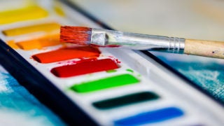 A brush sits atop a pallette of watercolor paint.