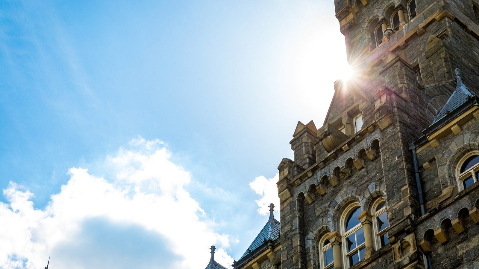 The sun flares from behind the Healy Hall clock tower