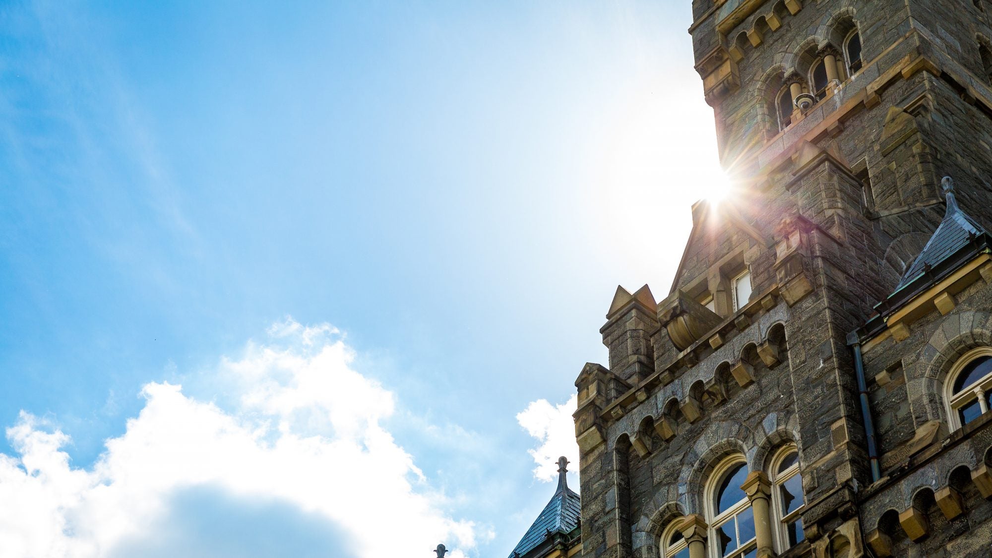 The sun flares from behind the Healy Hall clock tower