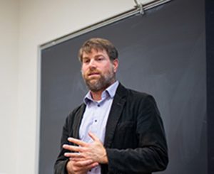 Adam Rothman stands in front of a classroom blackboard