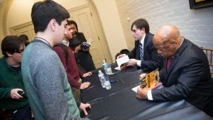 A student looks on as John Lewis signs a book as he sits beside Andrew Aydin. 