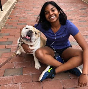Ashanee Kottage sits on the sidewalk smiling with Jack the Bulldog.
