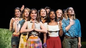 Ashanee Kottage stands in the middle of the front row of a group of women acting on stage.