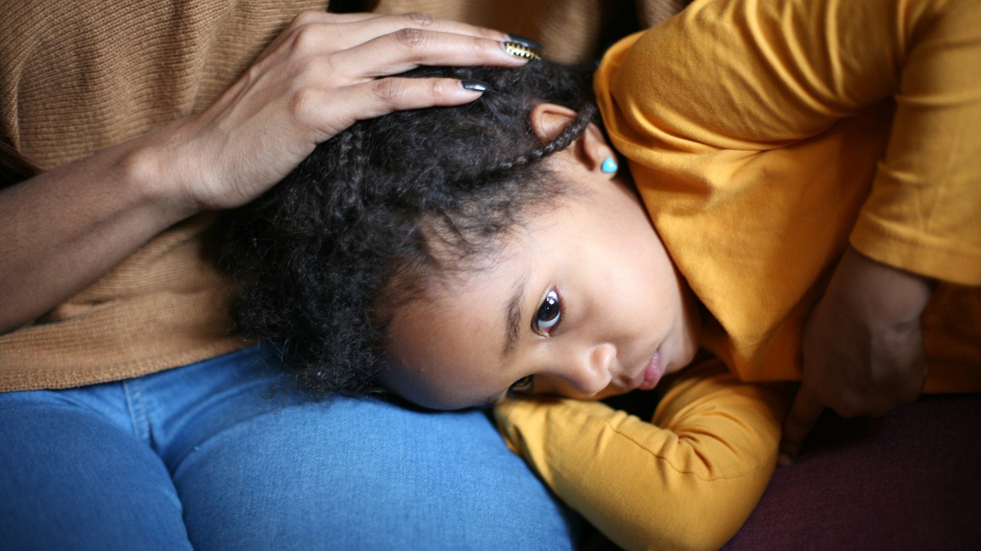 Child with her head on her mother&#039;s lap showing just the mother&#039;s hand on the girl&#039;s head