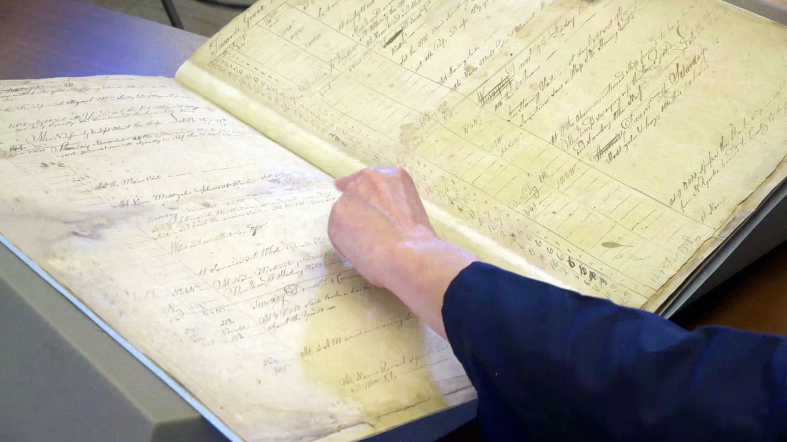 A woman flips through an old ship's logbook.