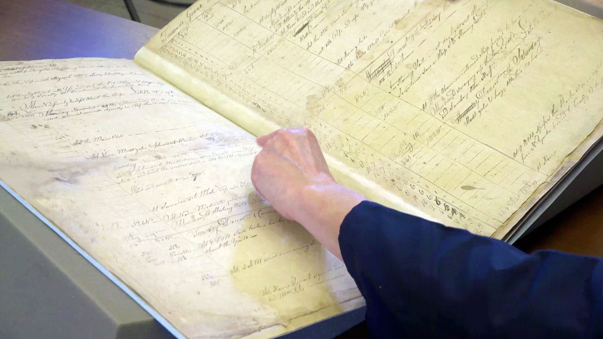 A woman flips through an old ship&#039;s logbook.