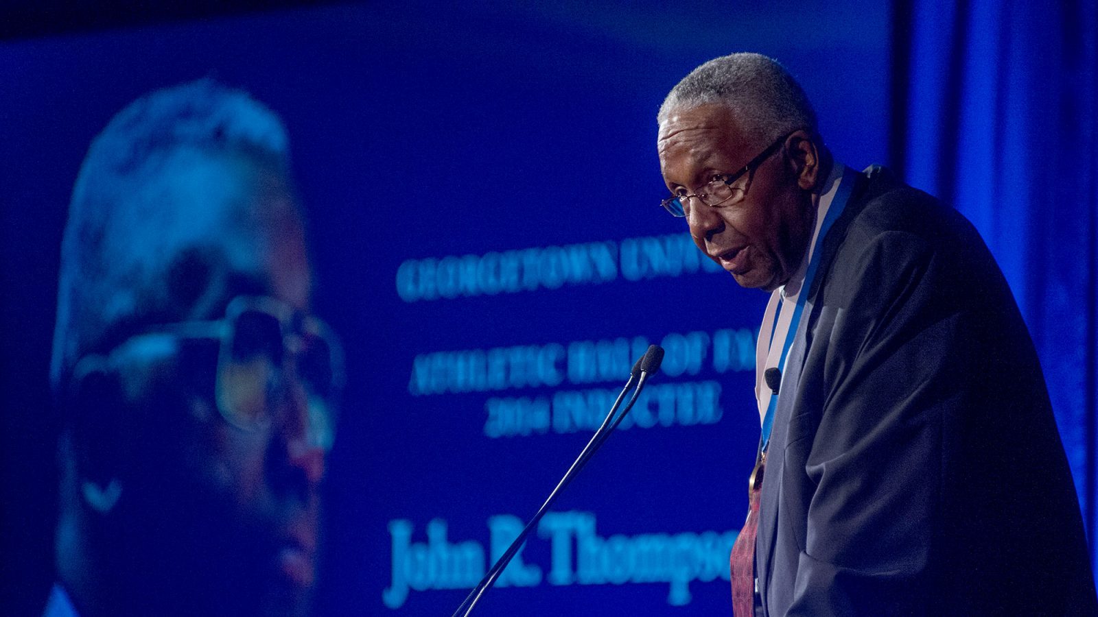John Thompson Jr. stands on stage with a tribute to him projected in the background.