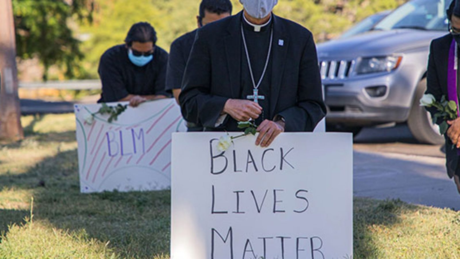 Clergy kneel holding Black Live Matter posters.