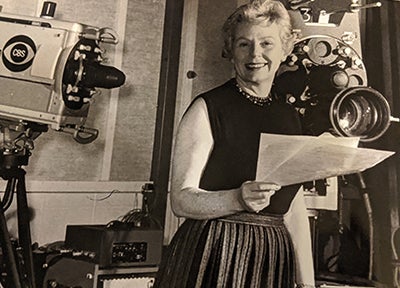 Lillian Brown standing and holding some papers in front of two CBS cameras in the late 1960s.