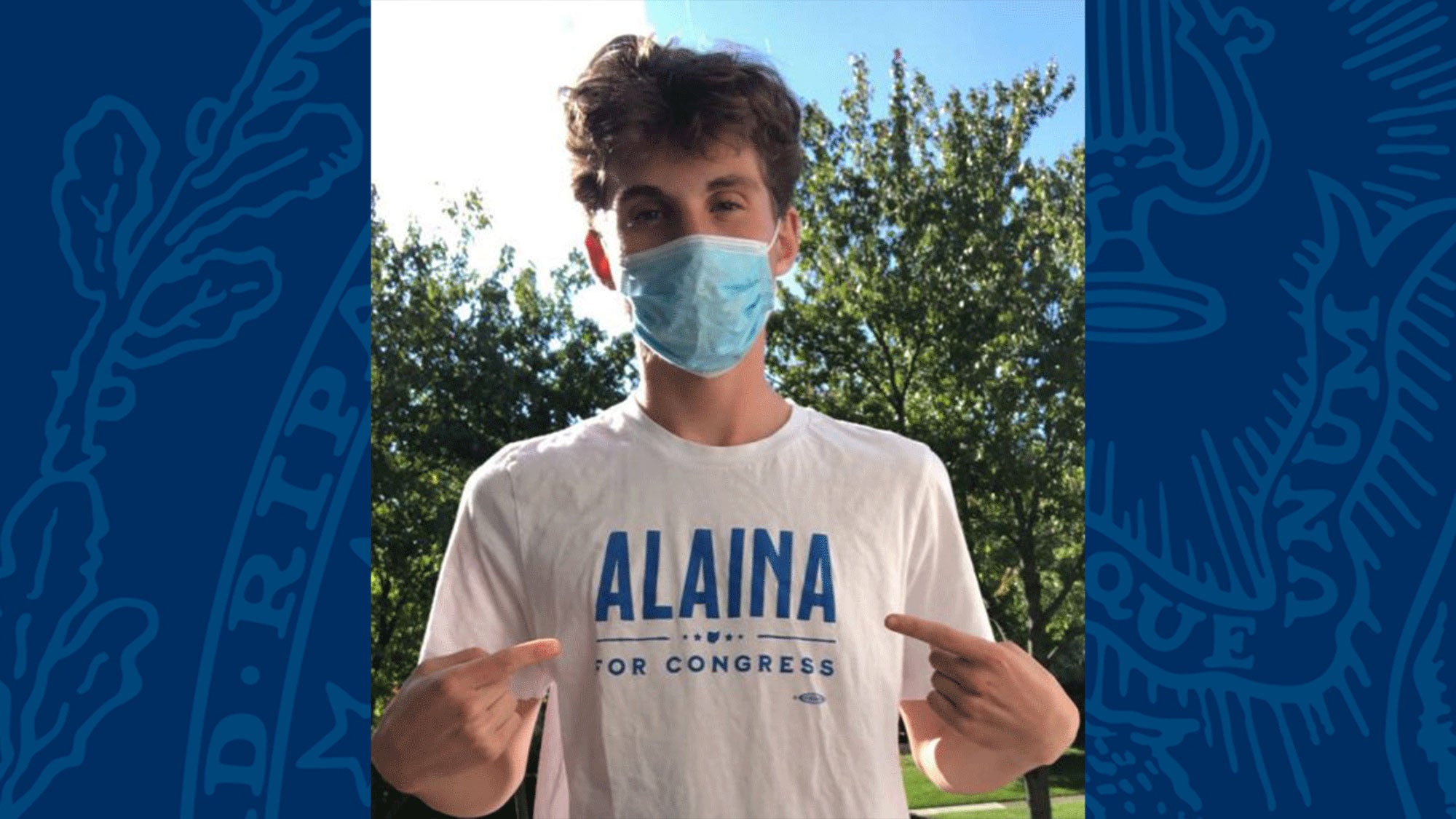 Charlie Sabgir stands pointing at his "Alaina For Congress" t-shirt.