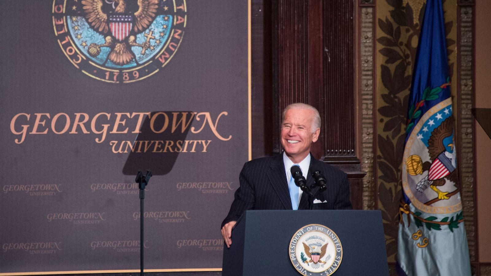 Joe Biden stands on the stage in Gaston Hall behind a lectern with a Georgetown University placard in the background.