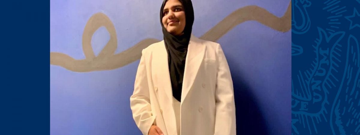 Khansa Maria stands against a wall wearing a white suit and black hijab.