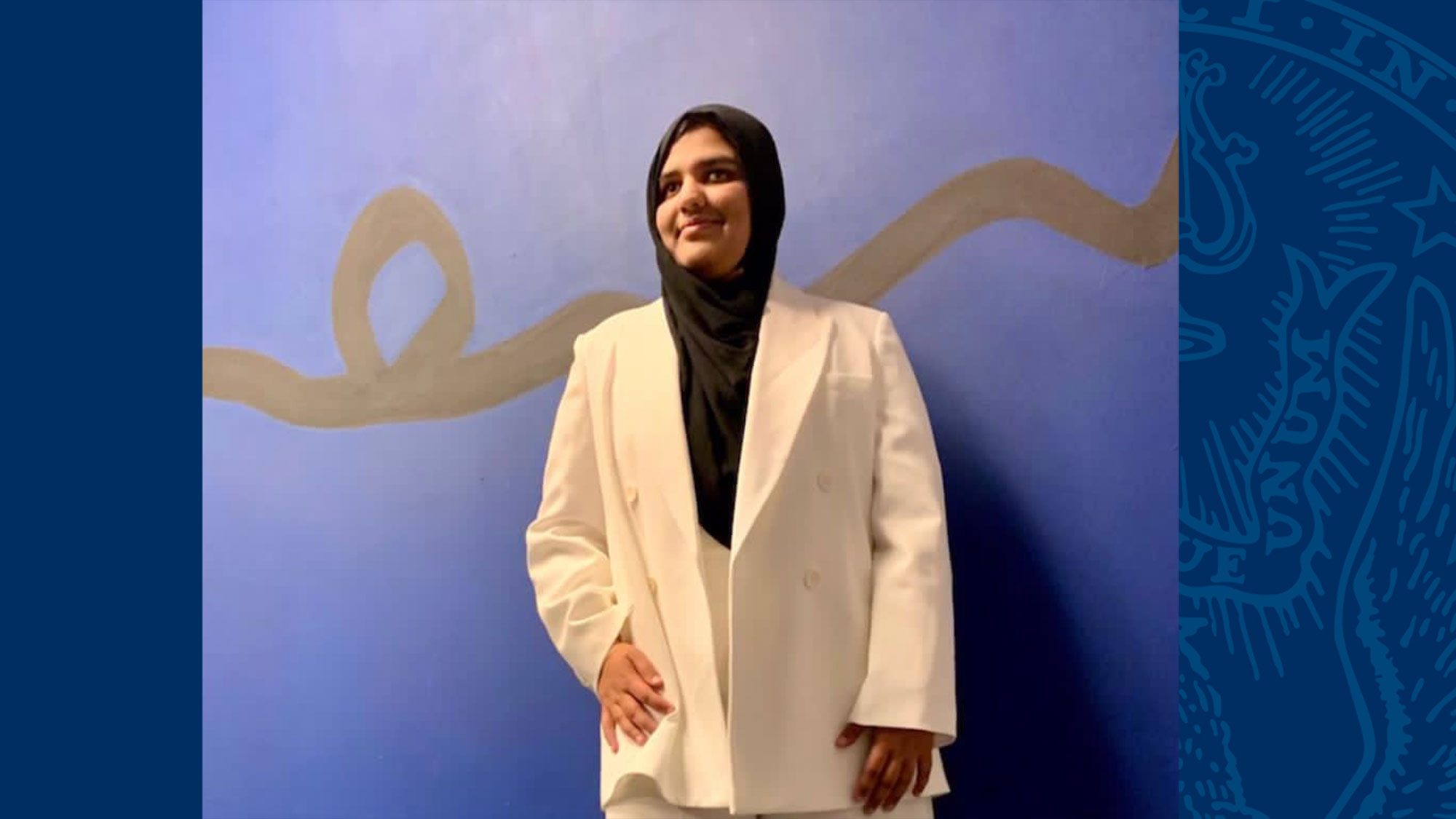 Khansa Maria stands against a wall wearing a white suit and black hijab.