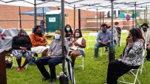 about 10 womenand men sit outside under a tent weraing masks outside.