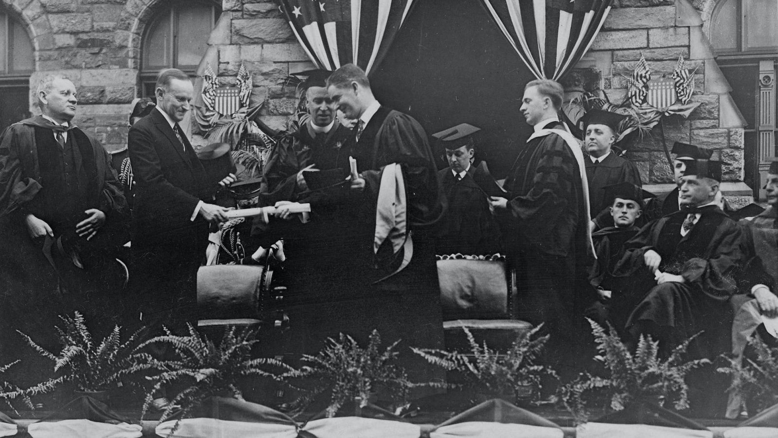 A black and white photo of President Calvin Coolidge participating in a Georgetown Commencement ceremony surrounded by individuals