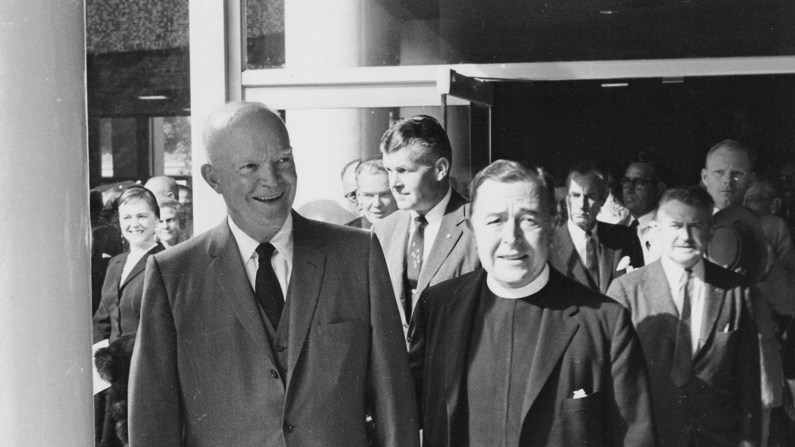 A black and white photograph of President Dwight Eisenhower exiting the Walsh Building with Father Edward B. Bunn