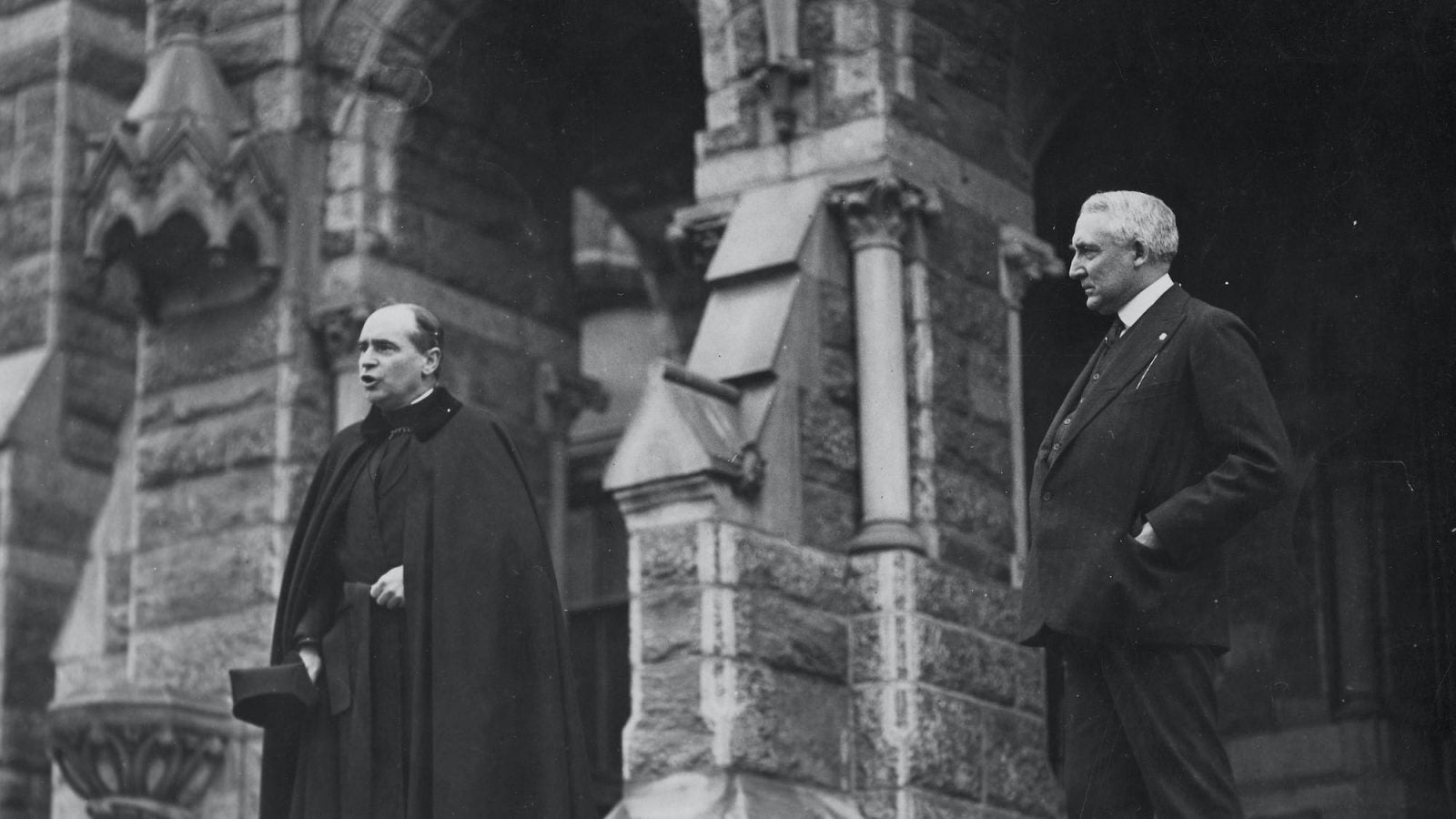 A black and white photo of President Warren Harding with a Jesuit priest on the step of Healy Hall